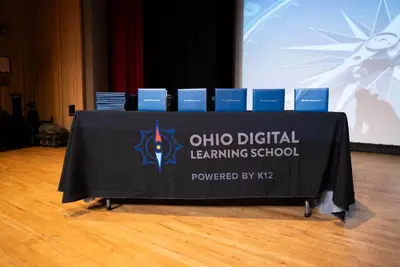 Una mesa con un mantel negro con el logotipo de la Escuela de Aprendizaje Digital de Ohio está coronada por diplomas azules ordenados.