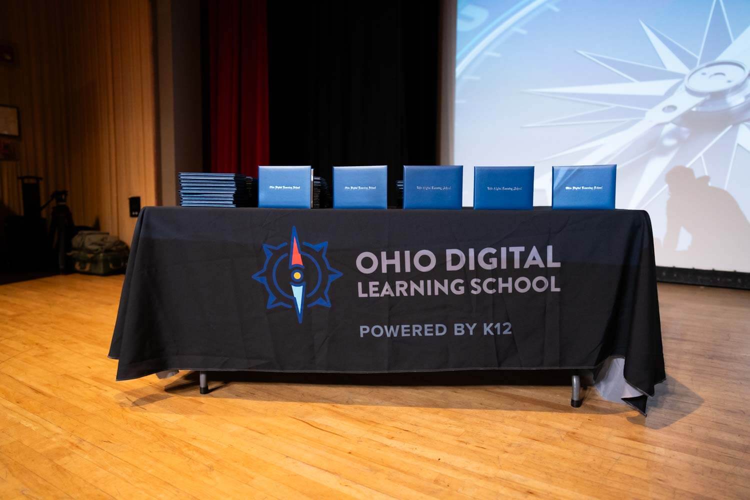 Una mesa con un mantel negro con el logotipo de la Escuela de Aprendizaje Digital de Ohio está coronada por diplomas azules ordenados.